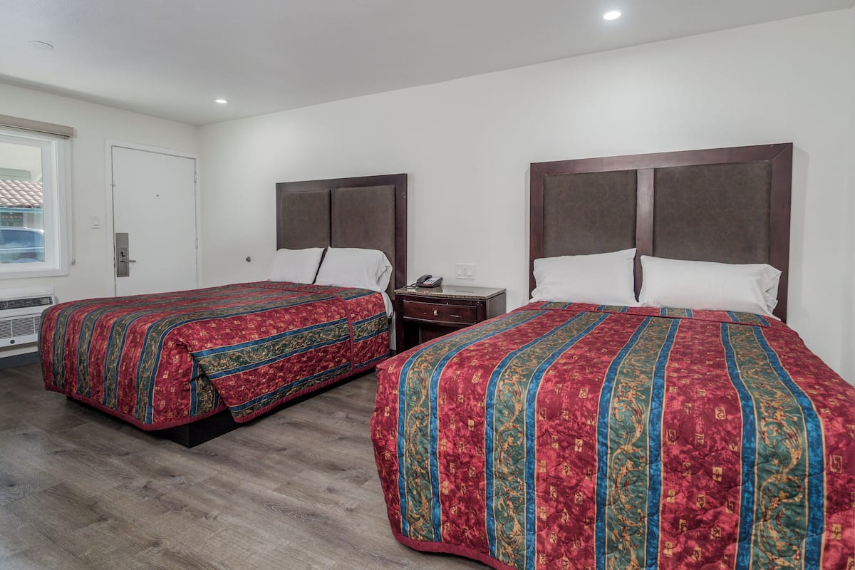 Habitación de hotel con dos camas, cada una con una colcha estampada, una mesita de noche con teléfono y una ventana con persianas.