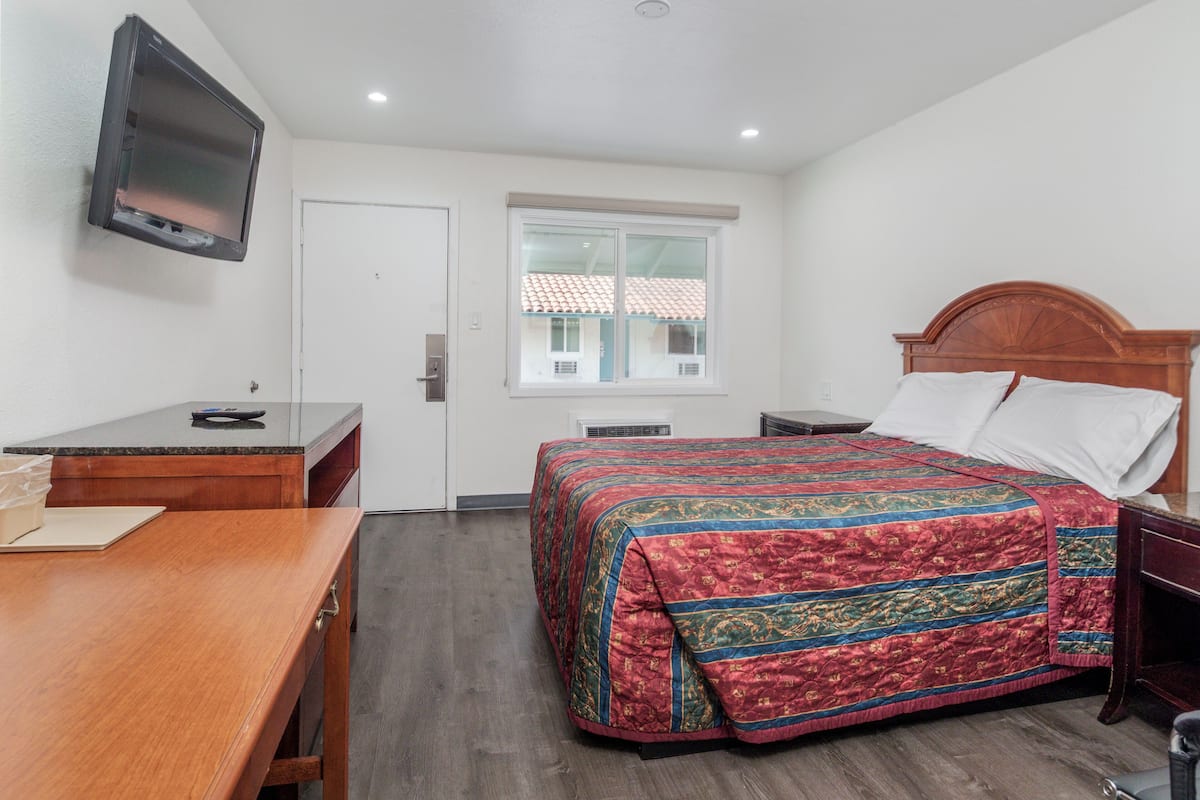 Una habitación de hotel con cama, escritorio, televisor y ventana.
