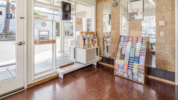 A room with a tiled floor, a bench, a display of books, and a wall with framed pictures. - The Alameda Motel San Jose (San Jose)