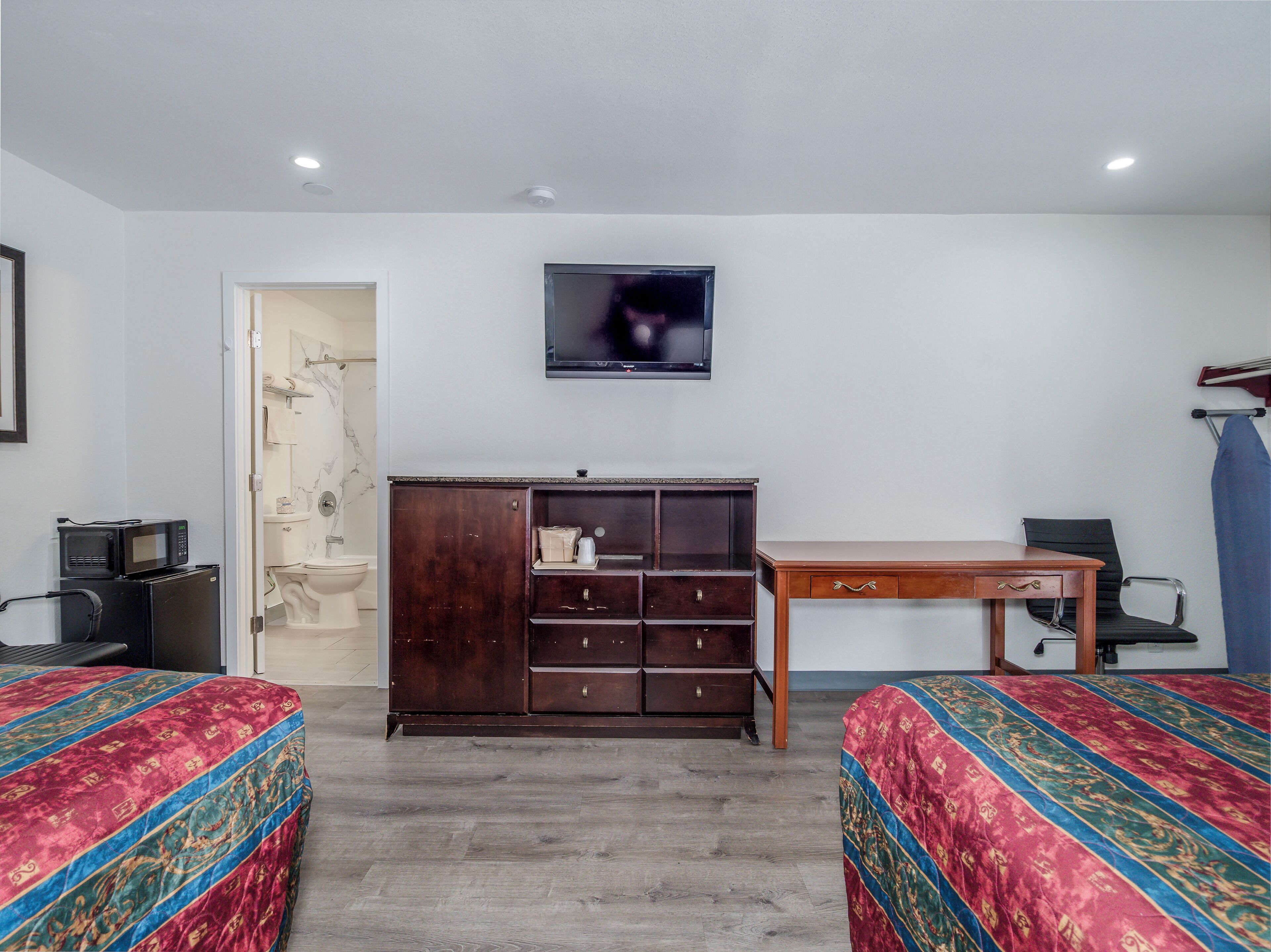 A hotel room with two beds, a wooden desk, a television, and a wardrobe.