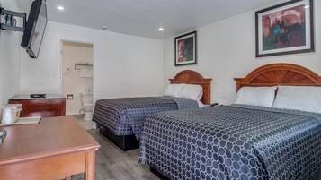 Quarto de hotel com duas camas, uma escrivaninha de madeira, televisão e banheiro visível por uma porta aberta.