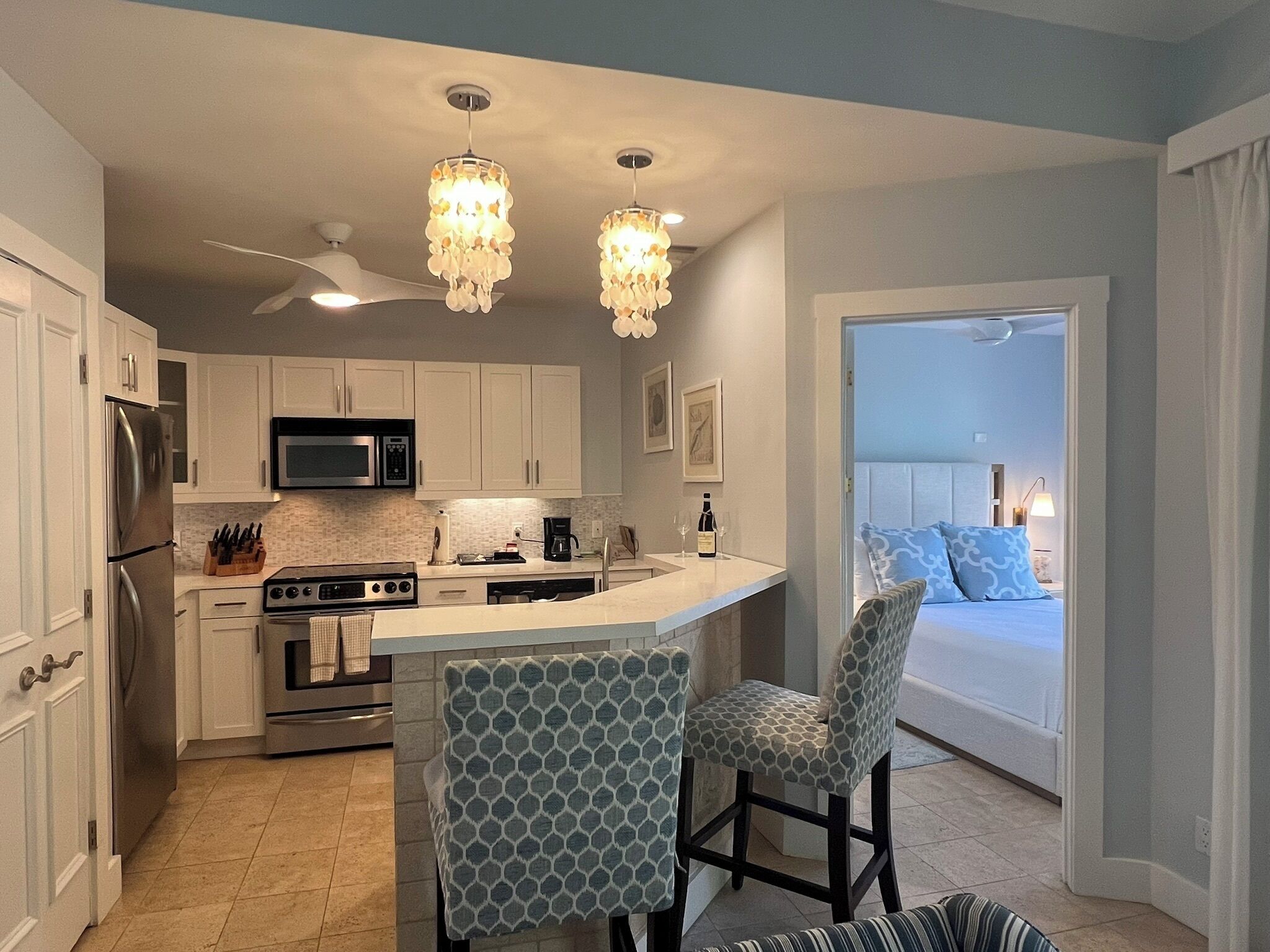 A modern kitchen with white cabinets, a central island, and two patterned chairs.
