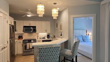 A modern kitchen with white cabinets, a central island, and two patterned chairs.