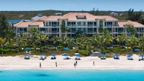 Ein Strandhotel mit mehreren Balkonen, einem Sandstrand und Palmen.