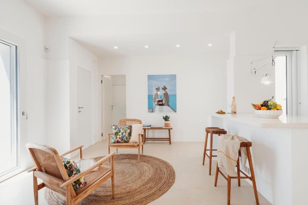A modern kitchen with a white countertop, wooden stools, and a woven rug.