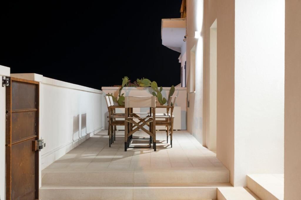 A balcony with a table and chairs, a door, and a white building.