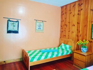 Cozy bedroom with a single bed, wooden headboard, and nightstand, featuring a vase of sunflowers and two decorative wall hangings.