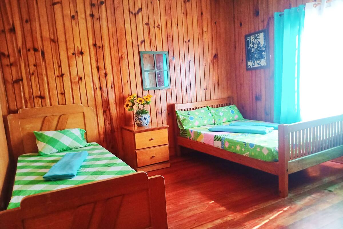 Ein Zimmer mit Holzboden, zwei Betten, einem Nachttisch und einem Wandbild.