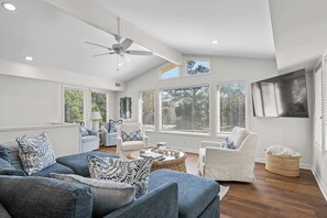 A modern living room with a ceiling fan, large windows with blinds, a sofa set, and a coffee table.