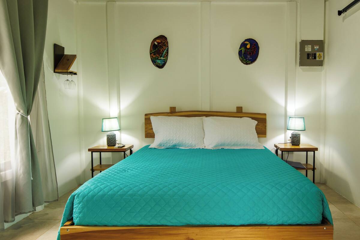 A neatly made bed with a teal bedspread, two bedside lamps, and decorative wall art.