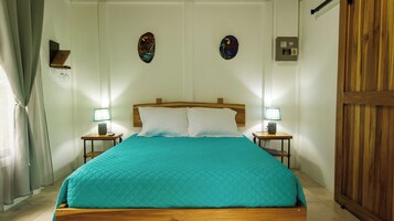 Una cama bien hecha con una colcha verde aguamarina, dos lámparas de noche y decoración en la pared.