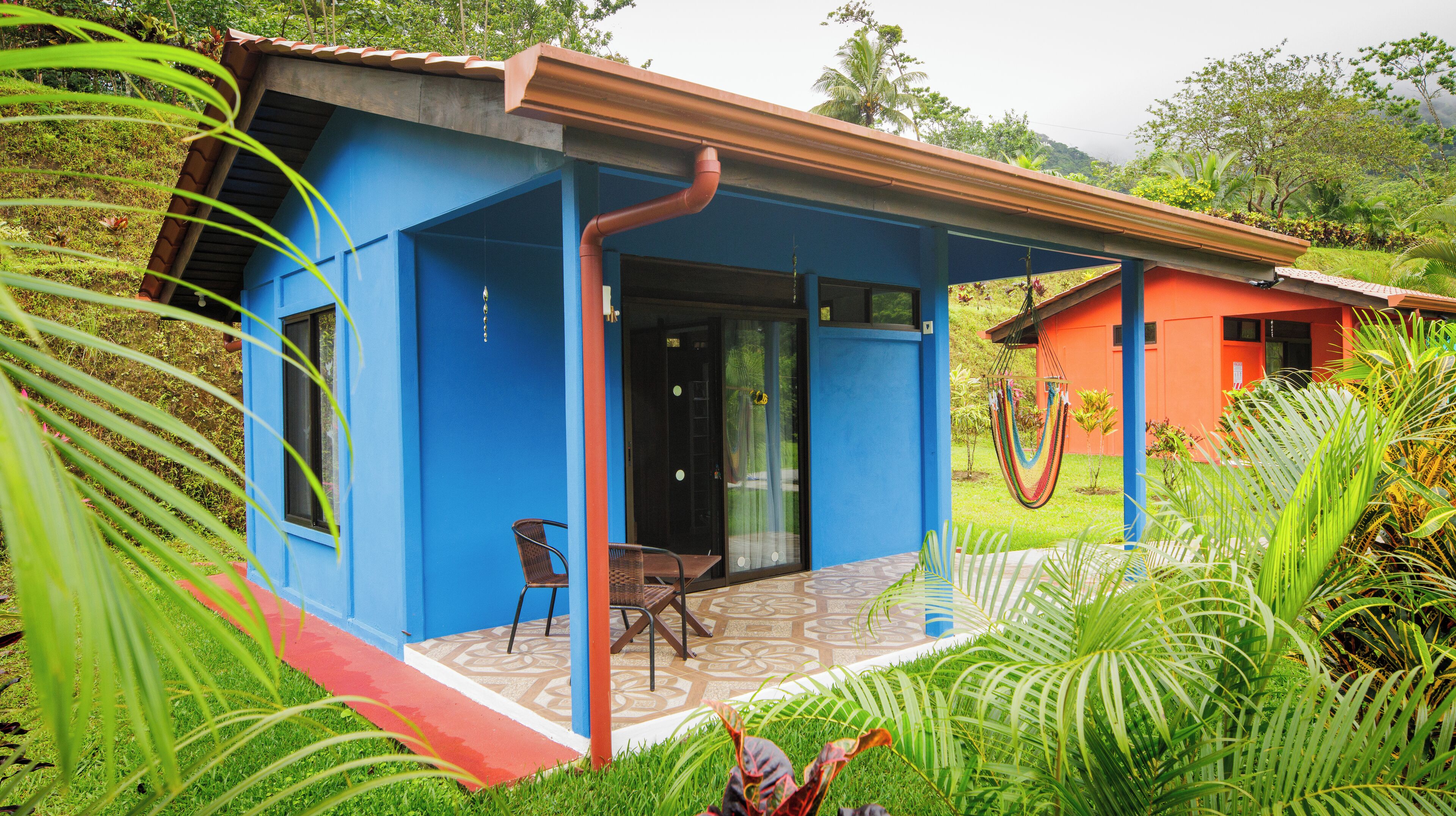 A blue and orange building with a covered porch, a chair, and a hammock.