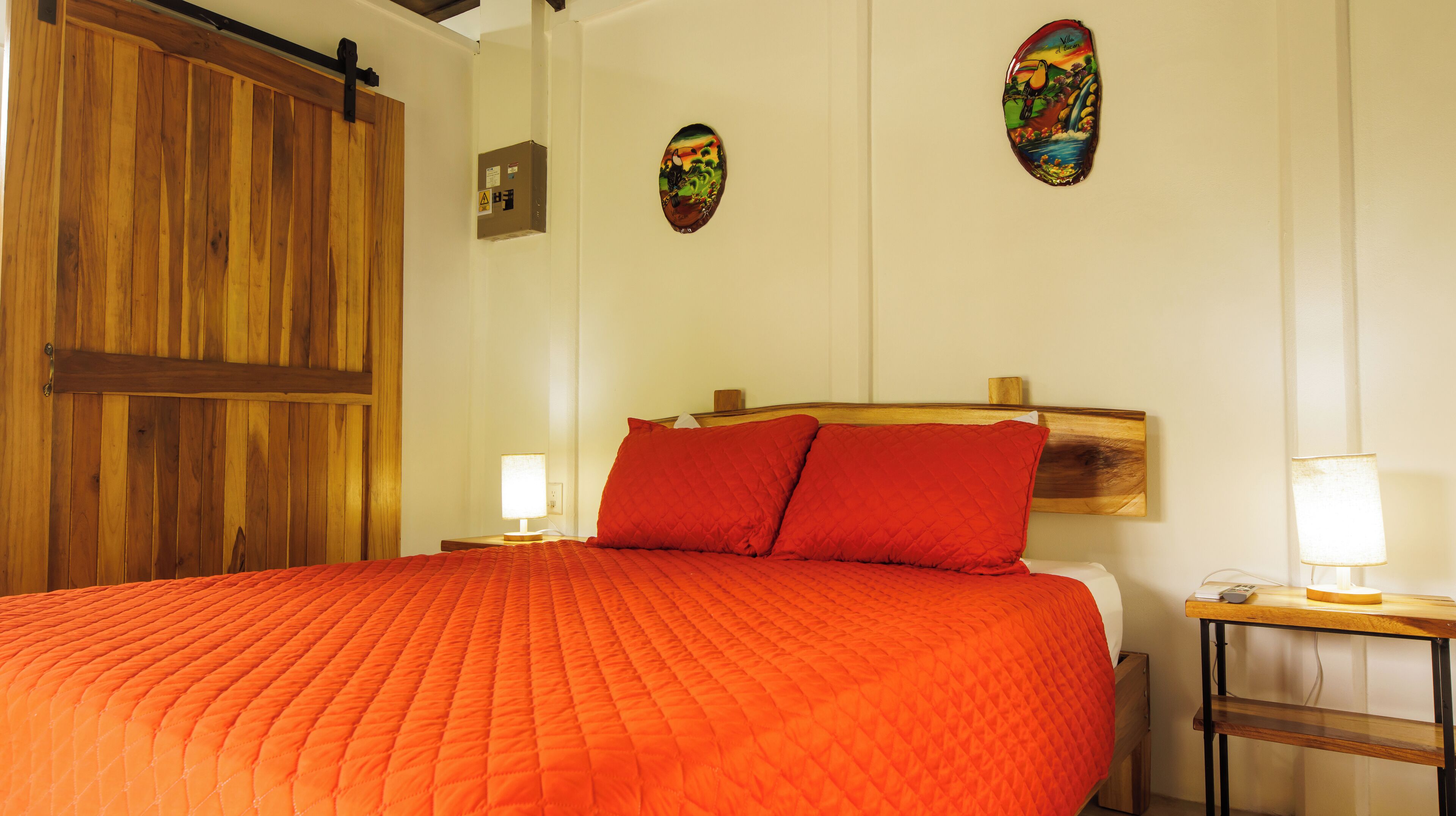 A bedroom with a large bed, wooden headboard, two bedside lamps, and a wooden door.