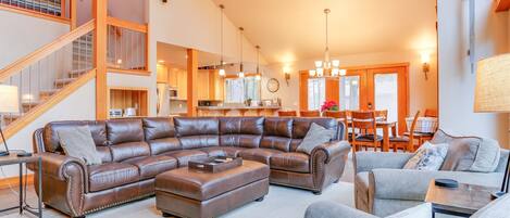 A spacious living room with a large L-shaped sectional sofa, a dining area with wooden furniture, and a staircase leading to an upper level.