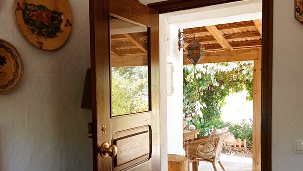 A wooden door leading to an outdoor patio with a table and chairs, surrounded by greenery. - Monte Alentejano Perto de Montemor-o-novo (Foros do Baldio)