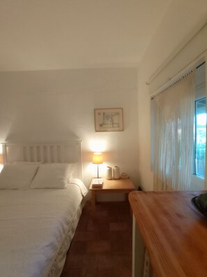 A bedroom with a bed, a bedside table with a lamp, a framed picture on the wall, and a window with curtains. - Monte Alentejano Perto de Montemor-o-novo (Foros do Baldio)