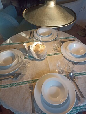 A round dining table set with white plates, bowls, glasses, and cutlery. A loaf of bread is placed in a bread basket on the table. - Monte Alentejano Perto de Montemor-o-novo (Foros do Baldio)