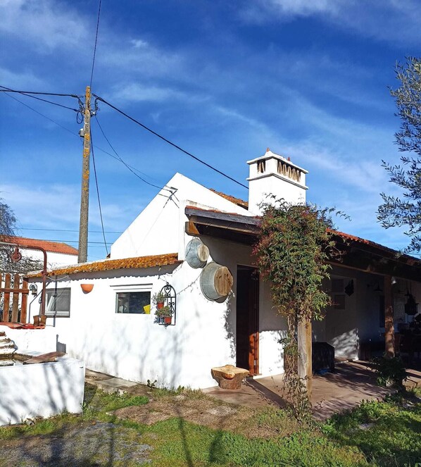 A white building with a tiled roof, a chimney, and a small porch with potted plants. - Monte Alentejano Perto de Montemor-o-novo (Foros do Baldio)