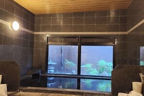 A spa room with a large window, dark tiled walls, and a wooden ceiling. - Hotel Route-Inn Kitakyushu-Wakamatsu Ekihigashi (Kitakyushu City)