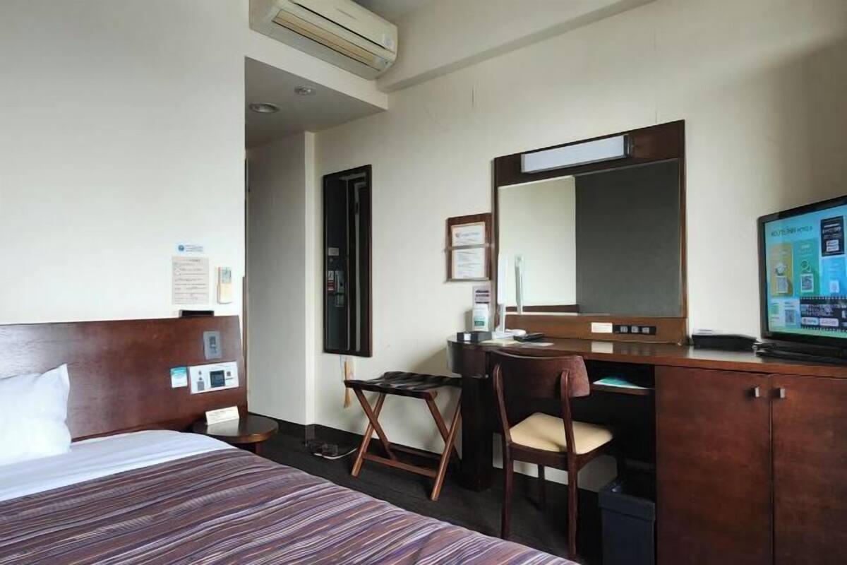 A hotel room with a bed, desk, chair, TV, and a mirror.