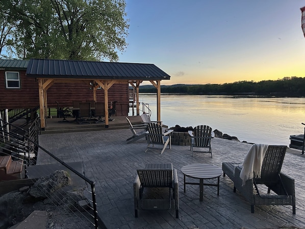 A wooden deck with outdoor furniture, a covered seating area, and a view of a calm body of water.