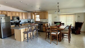Una cocina moderna con armarios de madera, electrodomésticos de acero inoxidable, una isla central con taburetes y un comedor con lámpara de araña.