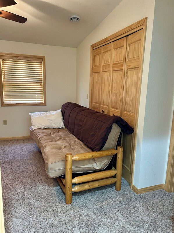 A compact room with a wooden-framed sofa, a window with blinds, and a wooden wardrobe.