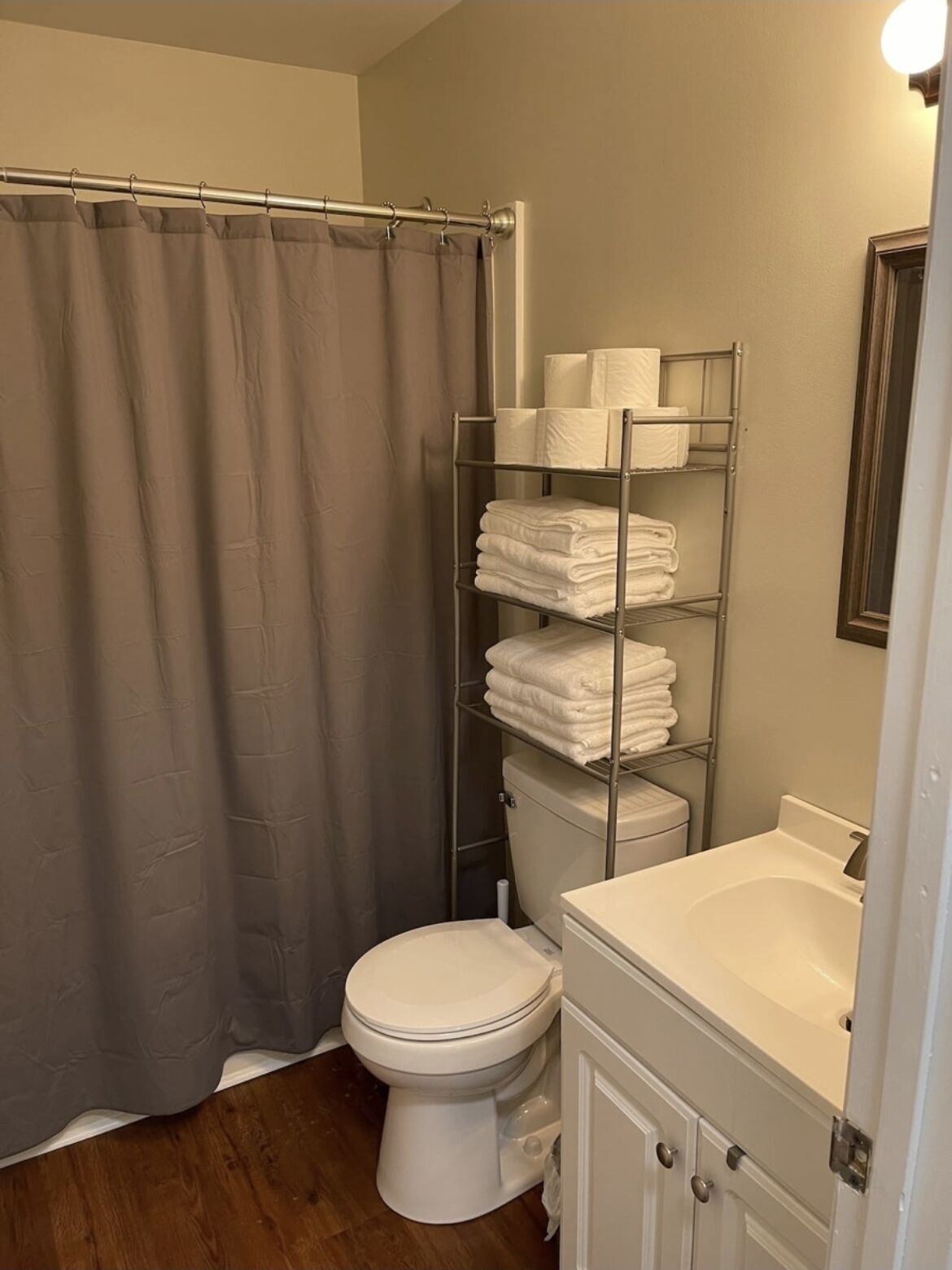 A bathroom with a shower curtain, a toilet, a sink, and a metal shelf with towels.