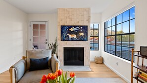 Una sala de estar con chimenea, un sofá, una estantería y un amplio ventanal con vistas al exterior.