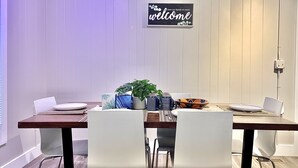 A dining area with a wooden table, white chairs, a welcome sign, and various decorative items.