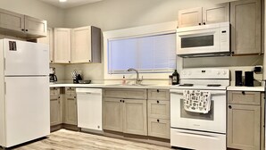A modern kitchen with white appliances, wooden cabinets, a dishwasher, and a window with blinds.
