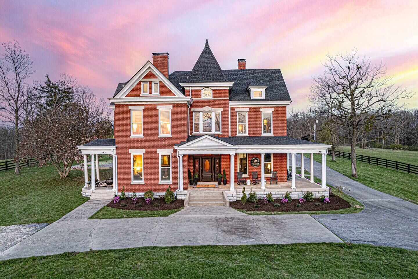 A large, two-story brick house with a wrap-around porch and a small garden area.