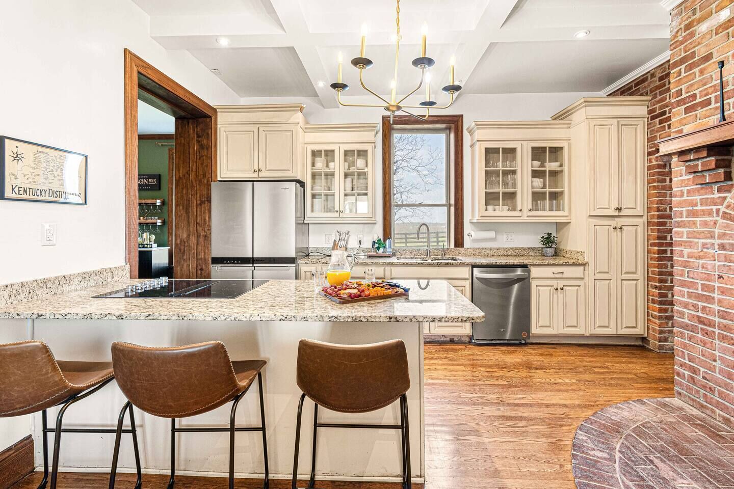 A modern kitchen with a central island, bar stools, stainless steel appliances, and a brick accent wall.