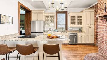 A modern kitchen with a central island, bar stools, stainless steel appliances, and a brick accent wall.