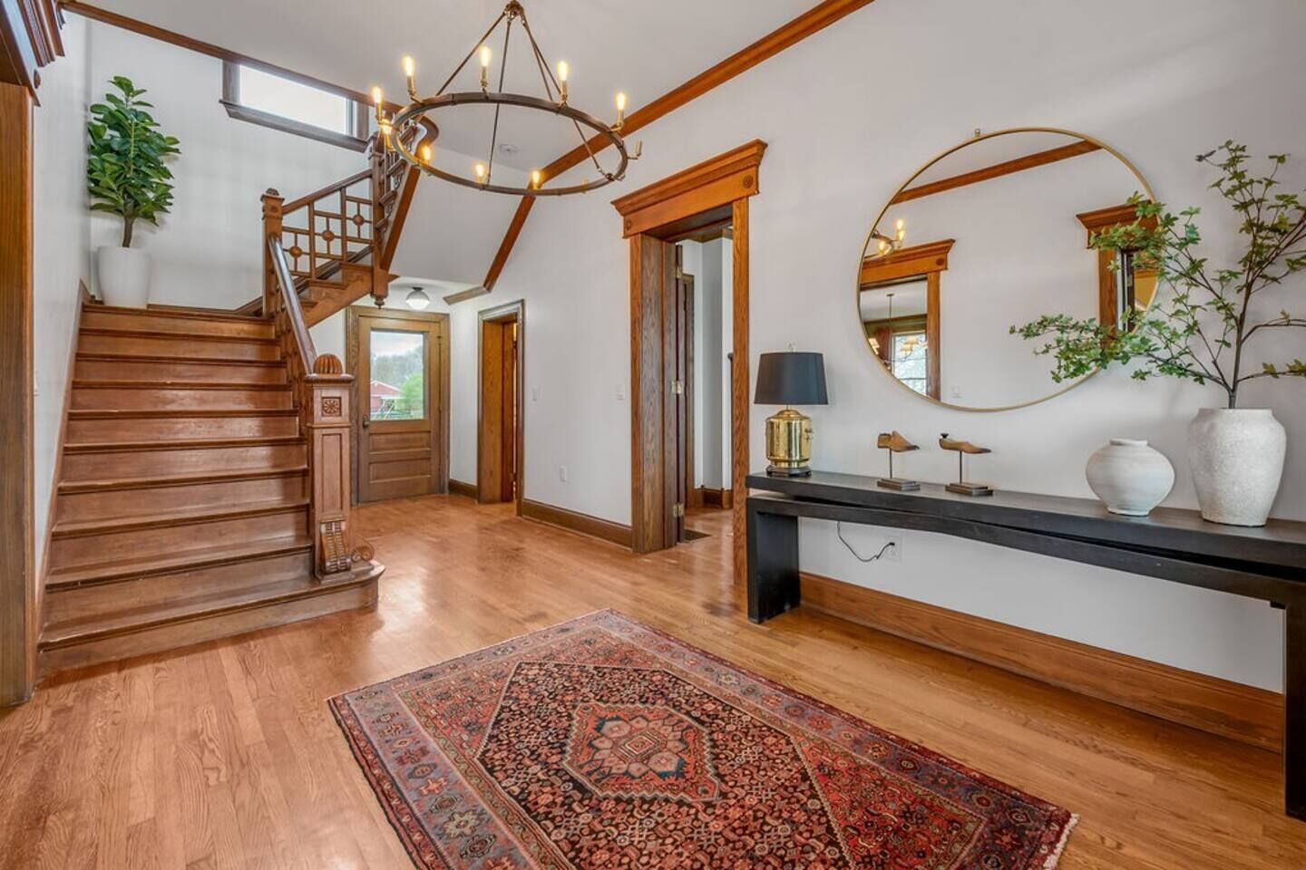 A spacious foyer with a wooden staircase, a large mirror, a console table, and a patterned rug.