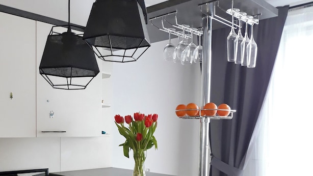 A modern kitchen with a central island, black bar stools, a vase with red flowers, and a wine rack. - Modern Calm Srudio, Wroclaw  (Wroclaw)