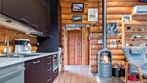 Une cuisine moderne aménagée dans un chalet en rondins, avec un poêle à bois, une machine à café et un plancher en bois.