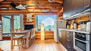 L’intérieur d’un chalet en bois comprend un coin repas, une cuisine et de grandes fenêtres donnant sur le paysage extérieur.