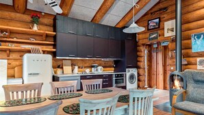 Une cuisine chaleureuse, aménagée dans le style d’un chalet, avec des murs en bois, une table à manger avec des chaises, un réfrigérateur, une cuisinière et un lave-linge.
