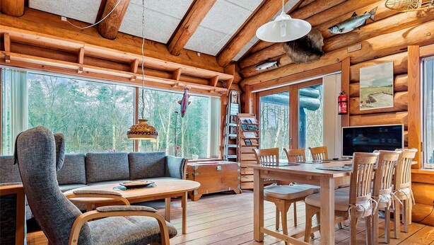 L’intérieur chaleureux d’un chalet avec une table à manger en bois, des chaises, un canapé et un téléviseur.