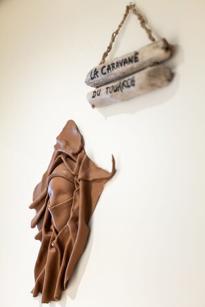 A white wall with two hanging items: a pair of wooden planks labeled "LA CARAVANE DU TOURNOIS" and a brown fabric draped over a surface.