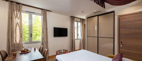 A bedroom with a bed, a desk with chairs, a TV, and a wardrobe.