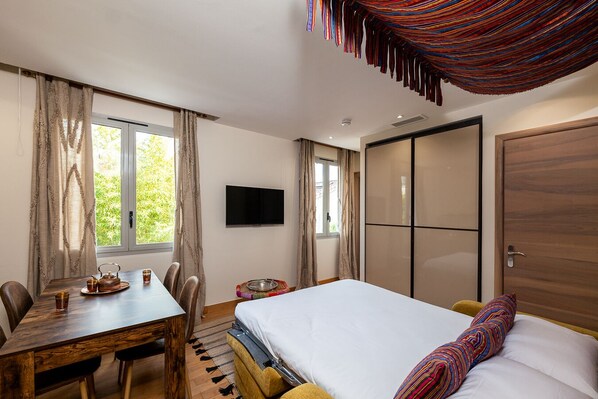 A bedroom with a bed, a desk with chairs, a TV, and a wardrobe.