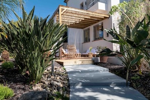 Eine Terrasse mit einer Holzpergola, Sitzgelegenheiten im Freien und tropischen Pflanzen.