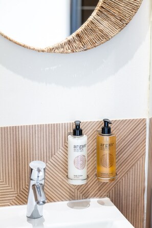 A bathroom with a wooden wall, a mirror, a sink, and two bottles of argan oil.