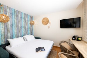A bedroom with a bed, a television, a desk, and a wicker chair.