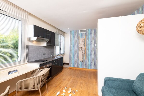A compact kitchen with modern appliances, a dining area with a chair, and a blue sofa.