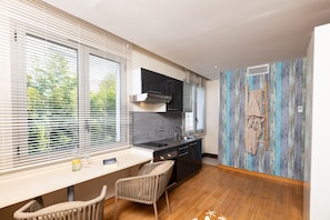 A modern kitchen with a dining area, large windows, and a rustic wall.