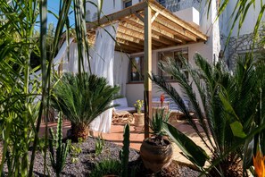 A covered outdoor seating area with a wooden pergola, potted plants, and a white curtain.