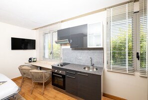 A compact kitchen with a built-in oven, a sink, and a flat-screen TV mounted on the wall.